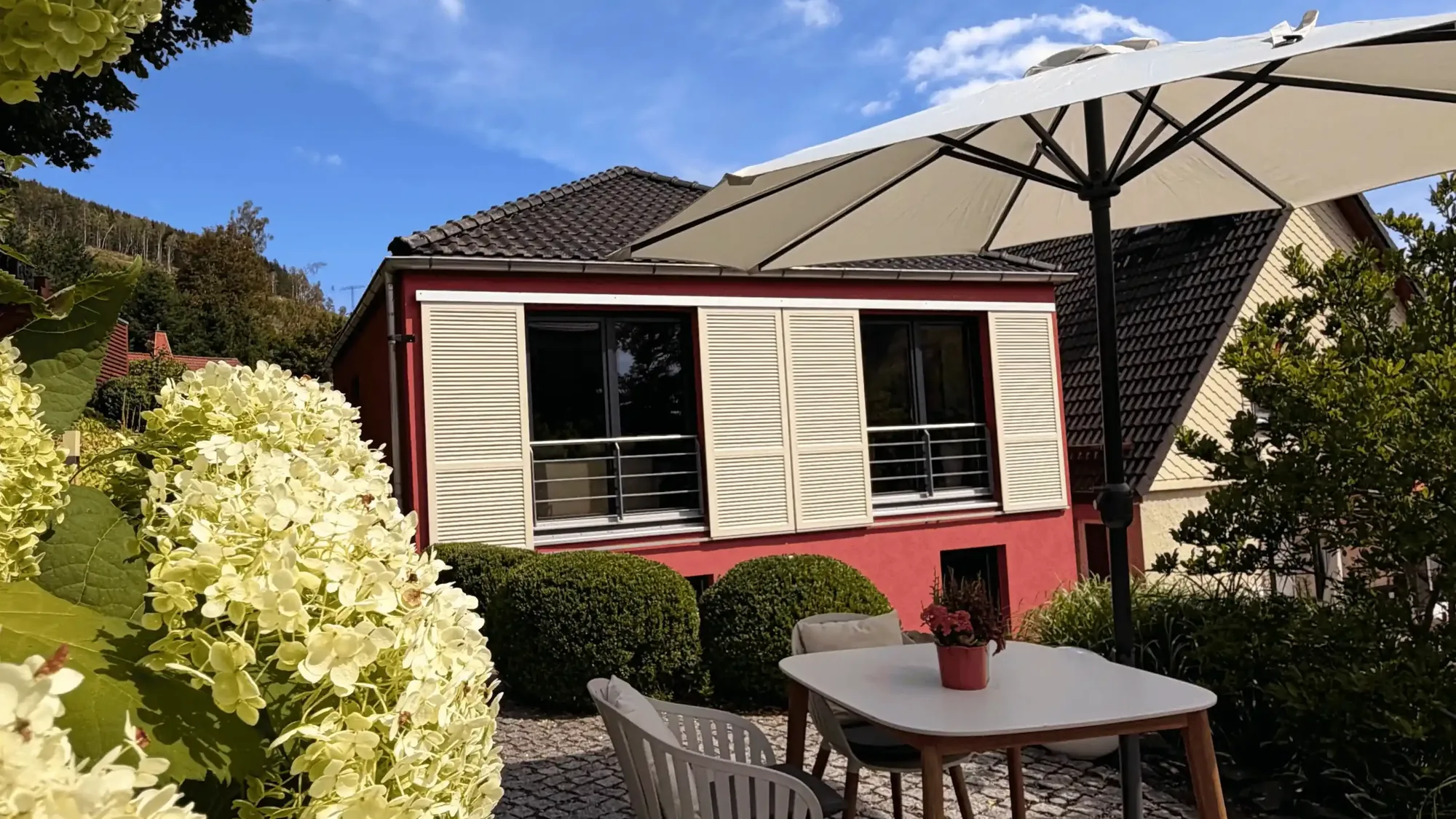 Terrasse am Ferienhaus Conradshöh mit Sonnenschirm, Tisch und Hortensien im Sommer