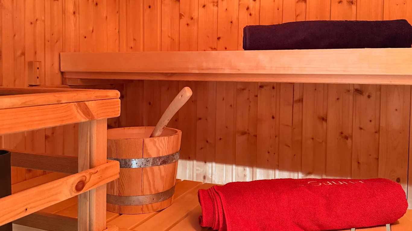 Innenraum der Sauna mit Holzbänken, Aufgusskübel und bereitgelegten Handtüchern